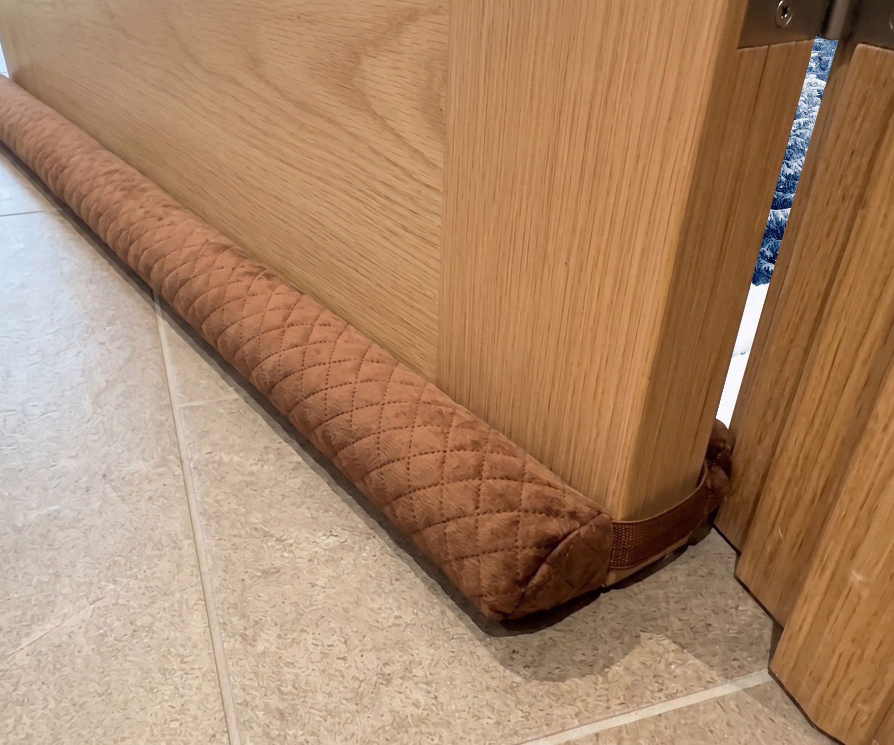 Twin Draft Guard Velvet in brown quilted velvet, installed under a wooden door on a tile floor
